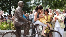 Olivia Chow, centro-direita, olha Sarah Layton e a sua filha Beatrice sentarem-se na estátua de bronze de Jack Layton - 22 de agosto de 2013. (The Canadian Press / Chris Young)