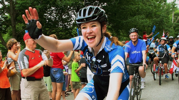 A “speedskater” olímpica canadiana e ciclista Clara Hughes acena, enquanto pedala com o governador-geral David Johnston (atrás) em Arnprior Ontário, na reta final da sua «Big Ride» - 30 de junho de 2014. (Fred Chartrand/The Canadian Press)