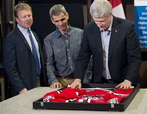 O primeiro-ministro Stephen Harper, à direita, coloca uma camisola de hóquei num porta-retrato, com o proprietário da loja Joe Mancino, ao centro, e o MP Rick Dykstra, durante uma oportunidade de foto na Framecraft Ltd., em St. Catharines, Ontário - quinta-feira, 22 de janeiro de 2015. The Canadian Press / Nathan Denette