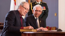 O mais recente primeiro-ministro da Prince Edward Island (P.E.I.), Wade MacLauchlan, assina o livro, sob a observação do tenente-Gov. da Prince Edward Island, Frank Lewis, durante uma cerimónia em Charlottetown - 23 de fevereiro de 2015. (John Morris / The Canadian Press)O mais recente primeiro-ministro da Prince Edward Island (P.E.I.), Wade MacLauchlan, assina o livro, sob a observação do tenente-Gov. da Prince Edward Island, Frank Lewis, durante uma cerimónia em Charlottetown - 23 de fevereiro de 2015. (John Morris / The Canadian Press)